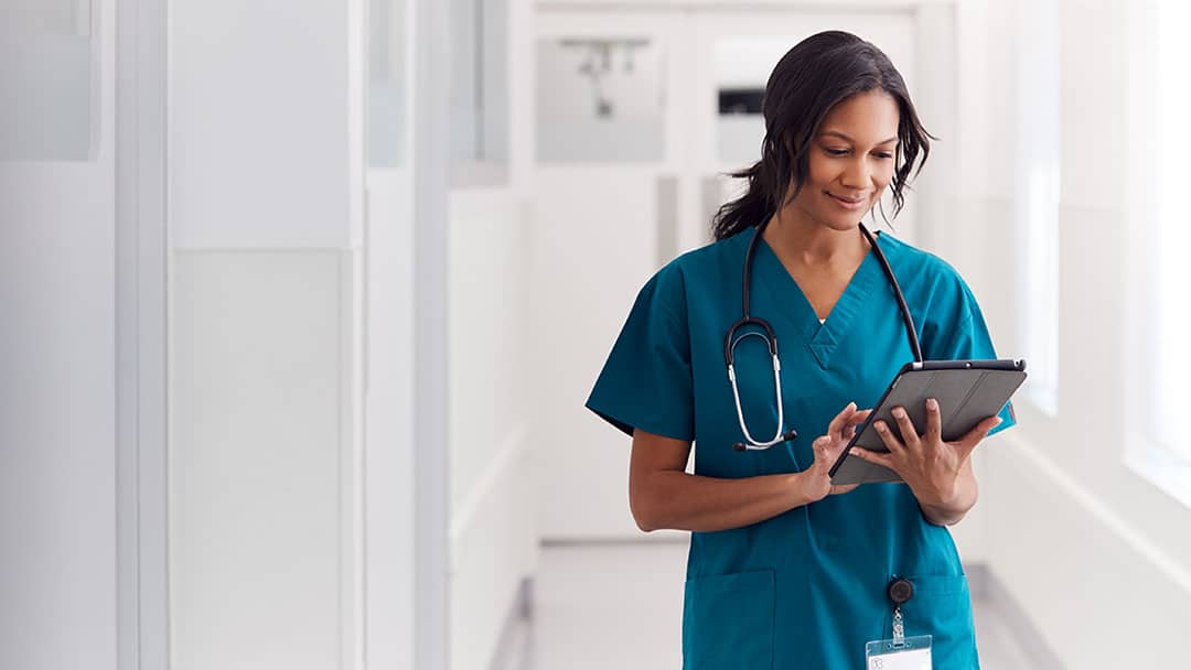 Nurse in a bright hallway reading records on a tablet device